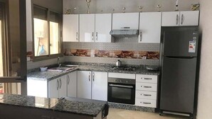 A modern kitchen with white cabinets, a granite countertop, a built-in oven, and a stainless steel refrigerator.