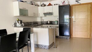 Una cocina moderna con armarios blancos, encimera de granito, refrigerador de acero inoxidable y un comedor con sillas negras.