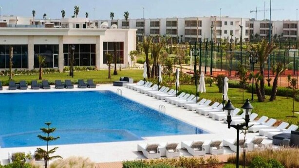 Una piscina con sillas de descanso y un edificio al fondo.