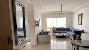 Amplia sala de estar con un sofá modular grande, un pequeño reposapiés, una mesa de comedor y un espejo grande.
