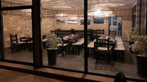 A restaurant with multiple tables and chairs, large potted plants, and a stone wall in the background. - Moroccan Surf Adventures 5185 (Imi Ouaddar)