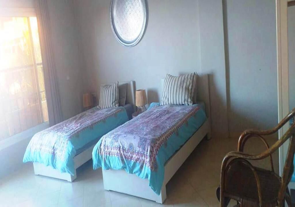 A bedroom with two beds, a round mirror, and a wooden chair.