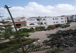 A white building with multiple balconies and a parking area in front.