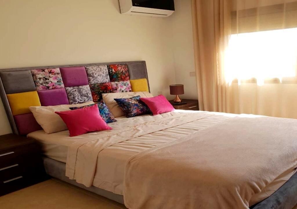 A neatly made bed with a variety of colorful pillows and a neutral-toned headboard.