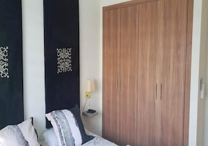 Een slaapkamer met een bed, nachtkastje, lamp en een kledingkast.