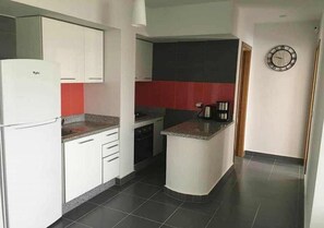 A compact kitchen with white cabinets, a built-in stove, and a red backsplash.