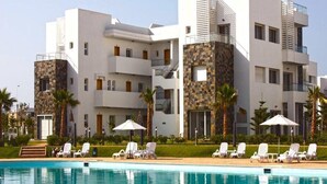Un hotel moderno con área de piscina, fachadas blancas y de piedra, y varios balcones.