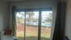 Habitación de hotel con cama, ventana con cortinas y vistas a una piscina y edificios.