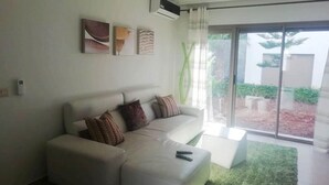 Una sala moderna con un sofá blanco, un televisor de pantalla plana y un amplio ventanal corredizo que da a un balcón.