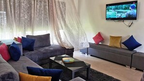 Ett modernt vardagsrum med en grå soffa, ett svart soffbord och en tv som är monterad på väggen.