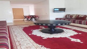 A living room with a round table, a sofa, and a TV on the wall.