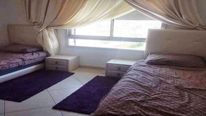 A bedroom with two beds, a window with curtains, a nightstand, and a purple rug.