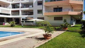 A multi-story building with a swimming pool, potted plants, and a well-maintained lawn.