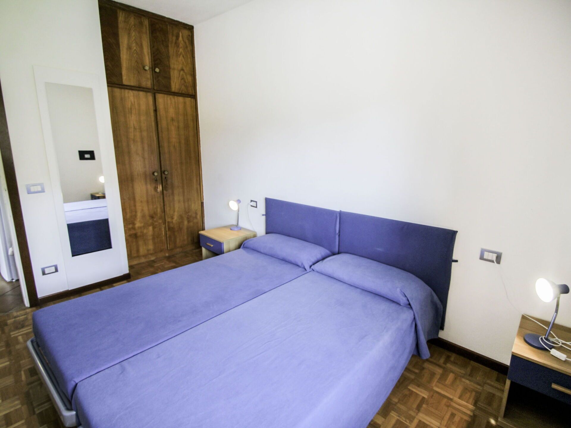 Een slaapkamer met een bed, een kledingkast, een nachtkastje en een lamp.