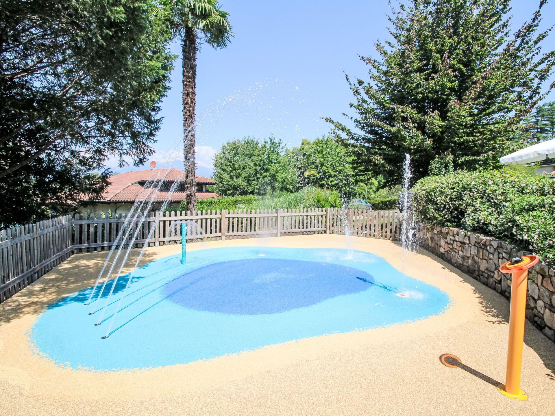 A swimming pool with a sandy bottom and a blue center, surrounded by a wooden fence and trees.