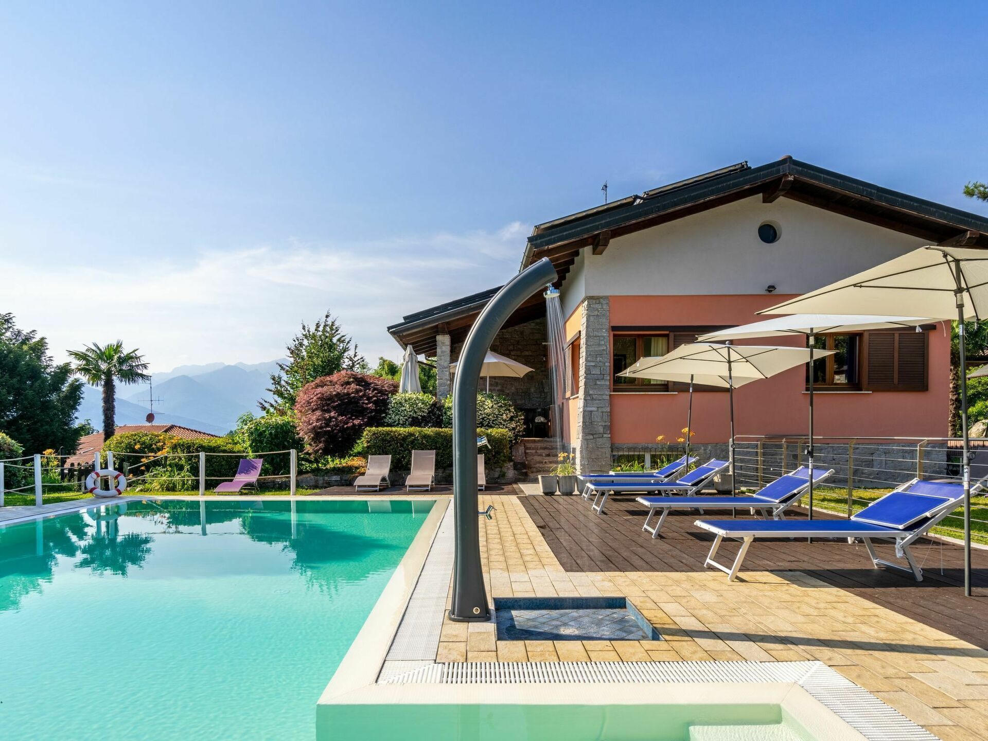 A swimming pool with lounge chairs and umbrellas, surrounded by a landscaped garden and a building with a stone facade.