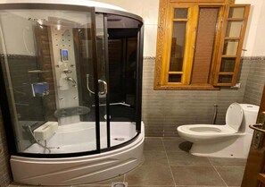 A bathroom with a glass-enclosed shower, a toilet, and a window with a wooden frame.