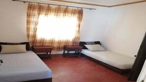 Ein Zimmer mit zwei Betten, einem kleinen Tisch und einem Fenster mit Vorhängen.
