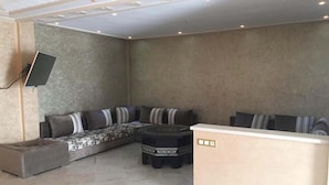 A modern lounge area with a sectional sofa, a round coffee table, and a flat-screen TV mounted on the wall. - Villa (Saidia)