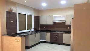 A modern kitchen with a central island, dark tiled backsplash, and stainless steel appliances. - Villa (Saidia)