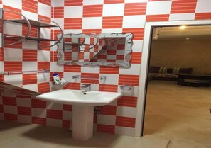 Une salle de bain avec un lavabo blanc, des carreaux rouges et blancs, un miroir et un espace douche.