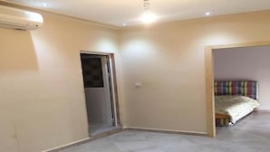 A room with a tiled floor, a door leading to another room, and a bed with a patterned bedspread. - Villa (Saidia)