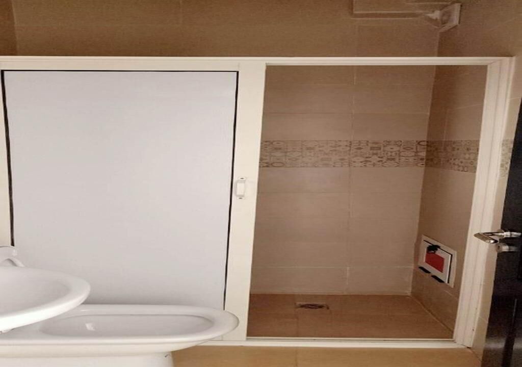 Ein Badezimmer mit Toilette in Weiß, einer Duschkabine mit beigen Fliesen und einem weißen Waschbecken.
