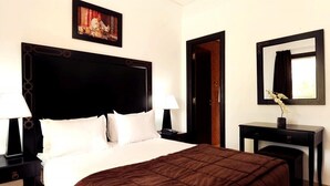 Ein Hotelzimmer mit einem großen Bett, zwei Nachttischen mit Lampen, einem Schminktisch und einer Tür.