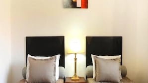 A hotel room with two beds, each with a black headboard, a bedside table with a lamp, and a small drawer. - Arz Village Farah Inn 4833 (Ifrane)