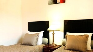 Ein Hotelzimmer mit zwei Betten, jeweils mit Kopfteil, einem Nachttisch mit Lampe und Kissen.