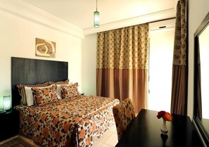 Ein Schlafzimmer mit einem Bett, einem Nachttisch, einem Tisch mit Blumen und Vorhängen.