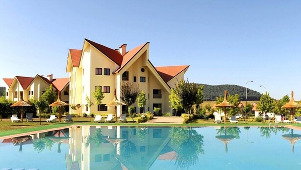 Un grande hotel con piscina di fronte, immerso nel verde sotto un cielo sereno.