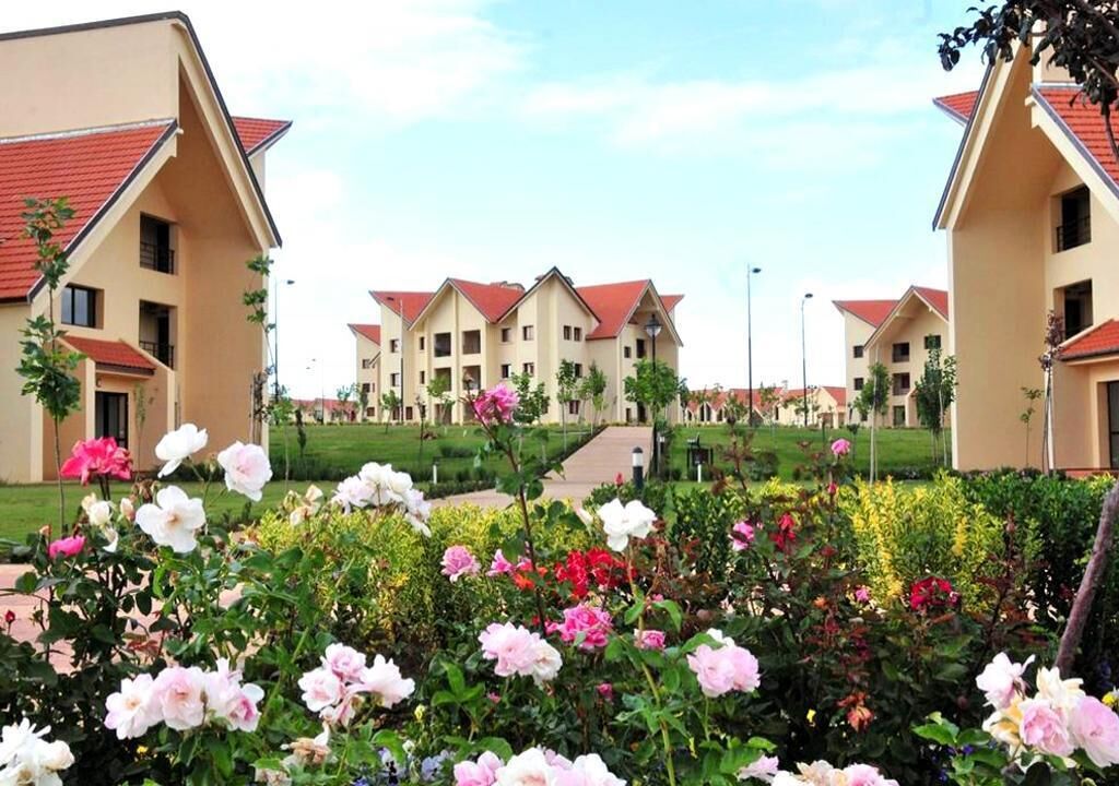 A residential building complex with multiple apartment buildings, a central pathway, and a well-maintained garden with various flowers.