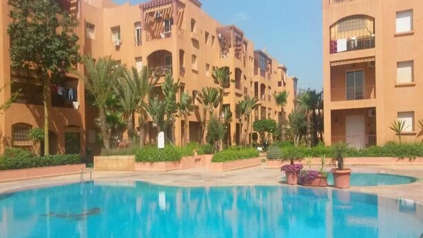 Una piscina rodeada de palmeras y un edificio con balcones.