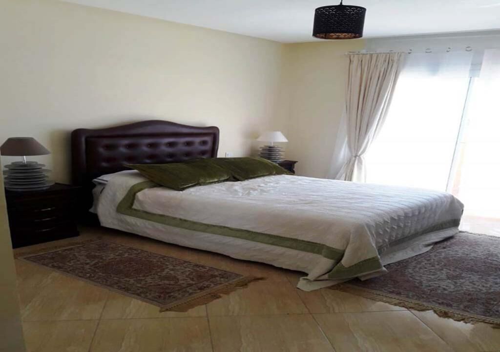 A bedroom with a bed, two bedside tables, a nightstand, a window with curtains, and a hanging light fixture.
