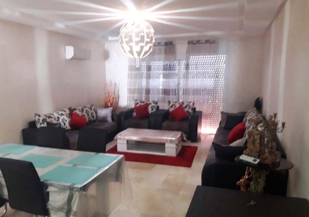A modern living room with a dining table, two sofas with red cushions, a coffee table, and a decorative plant.