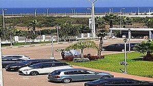 A parking lot with several cars, a grassy area with palm trees, and a view of the ocean in the background. - Superb apartment at Odyssée Bahia Beach Golf 4854 (Bouznika)