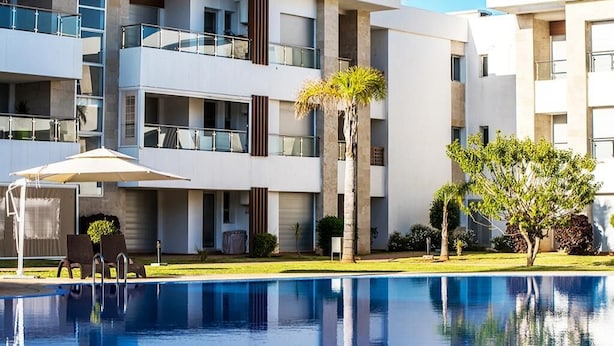 A modern multi-story hotel with a swimming pool, outdoor seating, and a well-maintained garden. - Superb apartment at Odyssée Bahia Beach Golf 4854 (Bouznika)