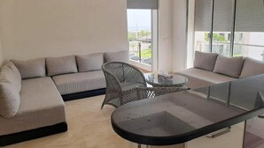 A modern living room with a sofa, a glass-top coffee table, and a wicker chair. - Superb apartment at Odyssée Bahia Beach Golf 4854 (Bouznika)