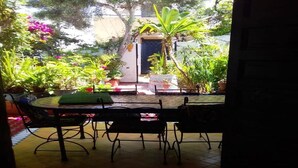 Un patio al aire libre con una mesa redonda y sillas, rodeado de plantas en macetas y un pequeño rincón con asientos.