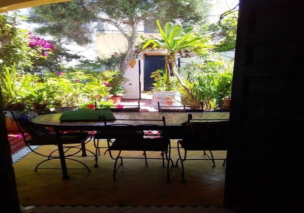 An outdoor patio area with a round table and chairs, surrounded by potted plants and a small seating area.