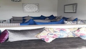 Una sala de estar moderna con un sofá modular, almohadones decorativos, un espejo montado en la pared y una lámpara de techo.