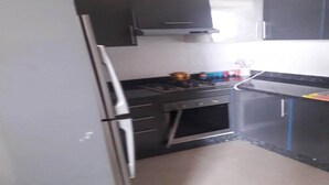 Una cocina compacta con refrigerador, estufa, horno y muebles oscuros.