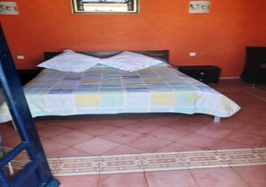Un lit simple avec une couvre-lit à motifs, une fenêtre au-dessus et un sol carrelé agrémenté d’une bordure décorative.