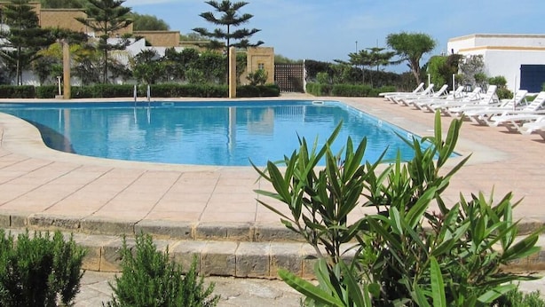 En swimmingpool med liggestole og en bygning i baggrunden.