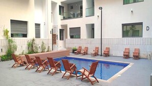 Une piscine avec des chaises longues, une terrasse carrelée et un bâtiment doté de plusieurs balcons.