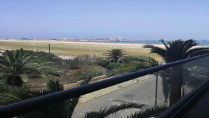 Une vue depuis un balcon donnant sur une plage bordée de palmiers et sur une ville lointaine.
