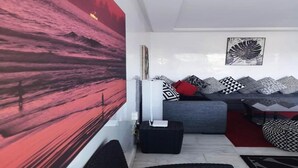Un salon moderne avec un grand tableau abstrait, un canapé gris agrémenté de coussins à motifs et un pouf noir.