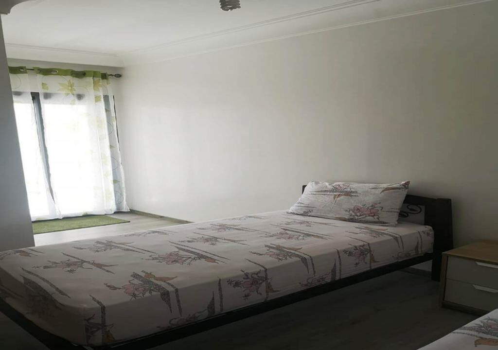 A single bed with floral bedding, a bedside table, and a window with curtains.