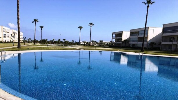 A swimming pool with clear blue water, surrounded by palm trees and modern buildings.